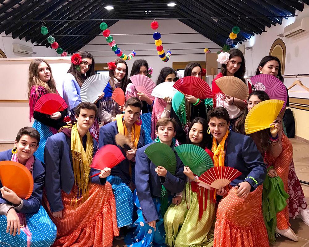 A group of students dressed in colorful flamenco costumes with fans, celebrating Spanish culture, in an indoor setting with decorations, showcasing cultural diversity and engagement.